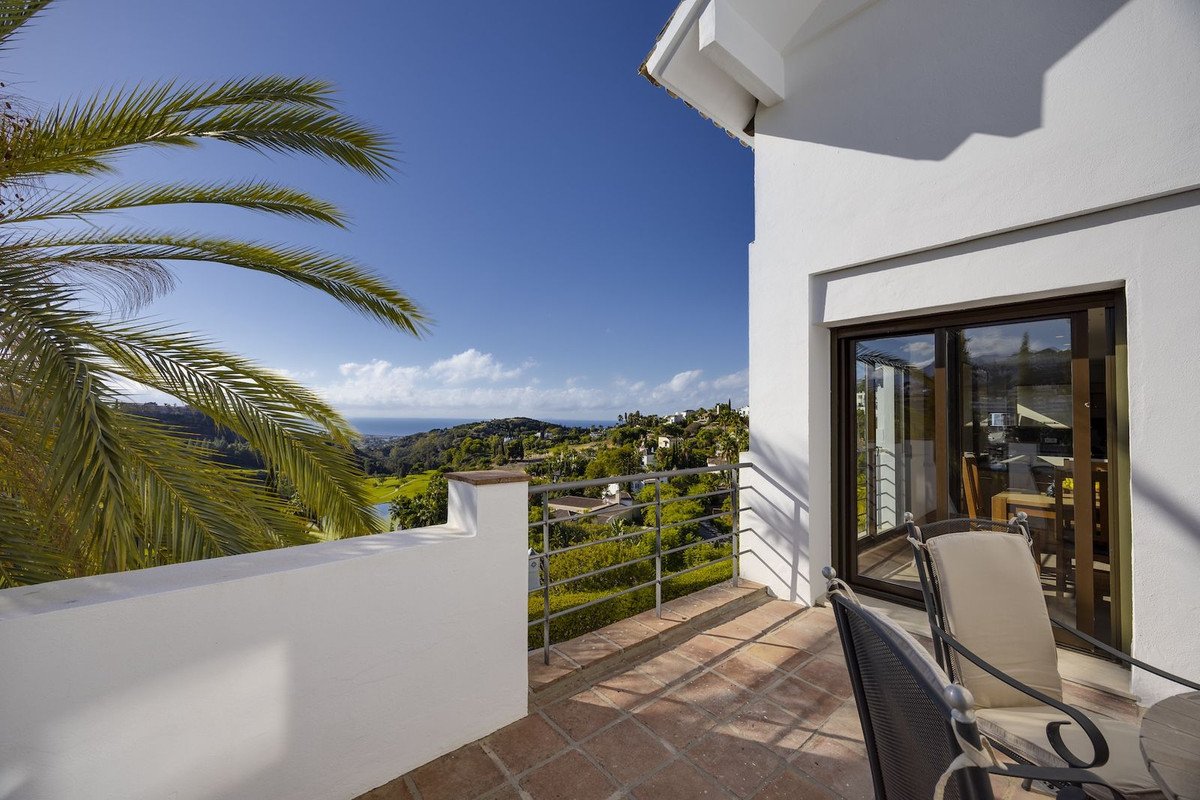 Terrace with sea and golf course view, palm trees, and outdoor seating, leading to a dining area inside.
