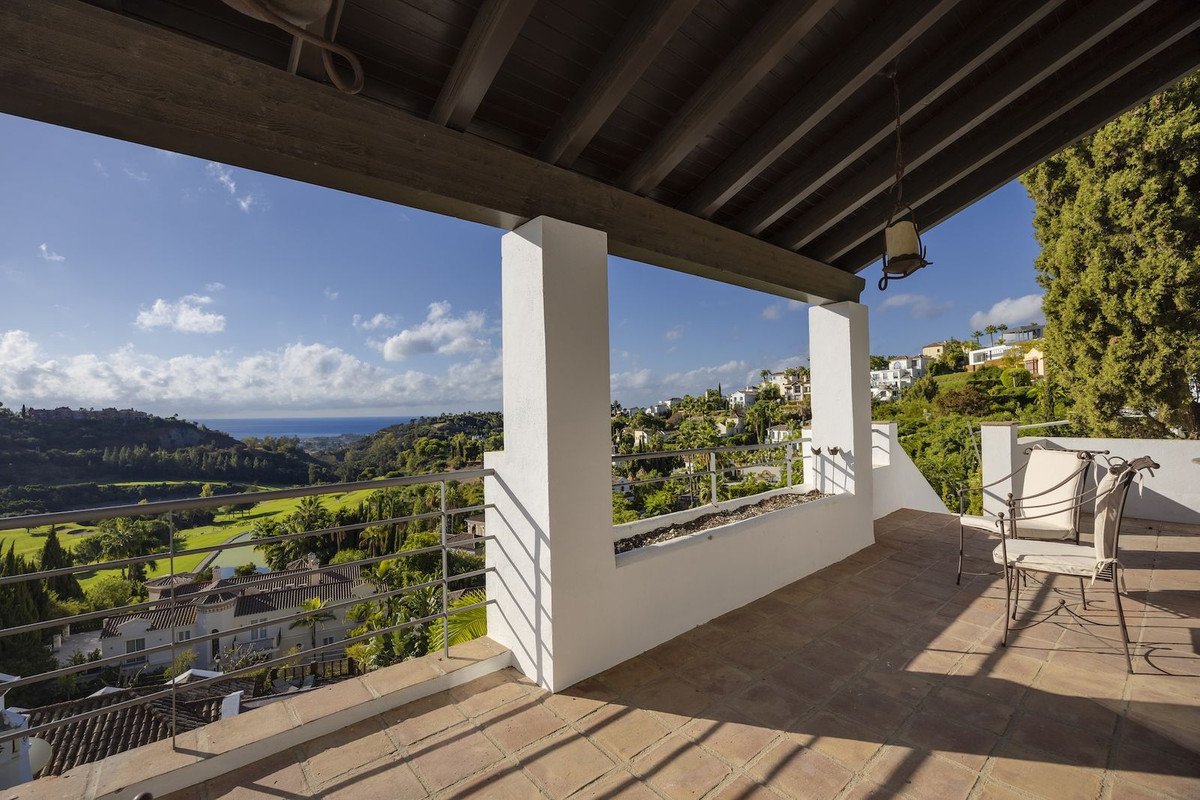 Terrace with seating, offering panoramic views of a golf course, lush greenery, and the distant sea under a blue sky.