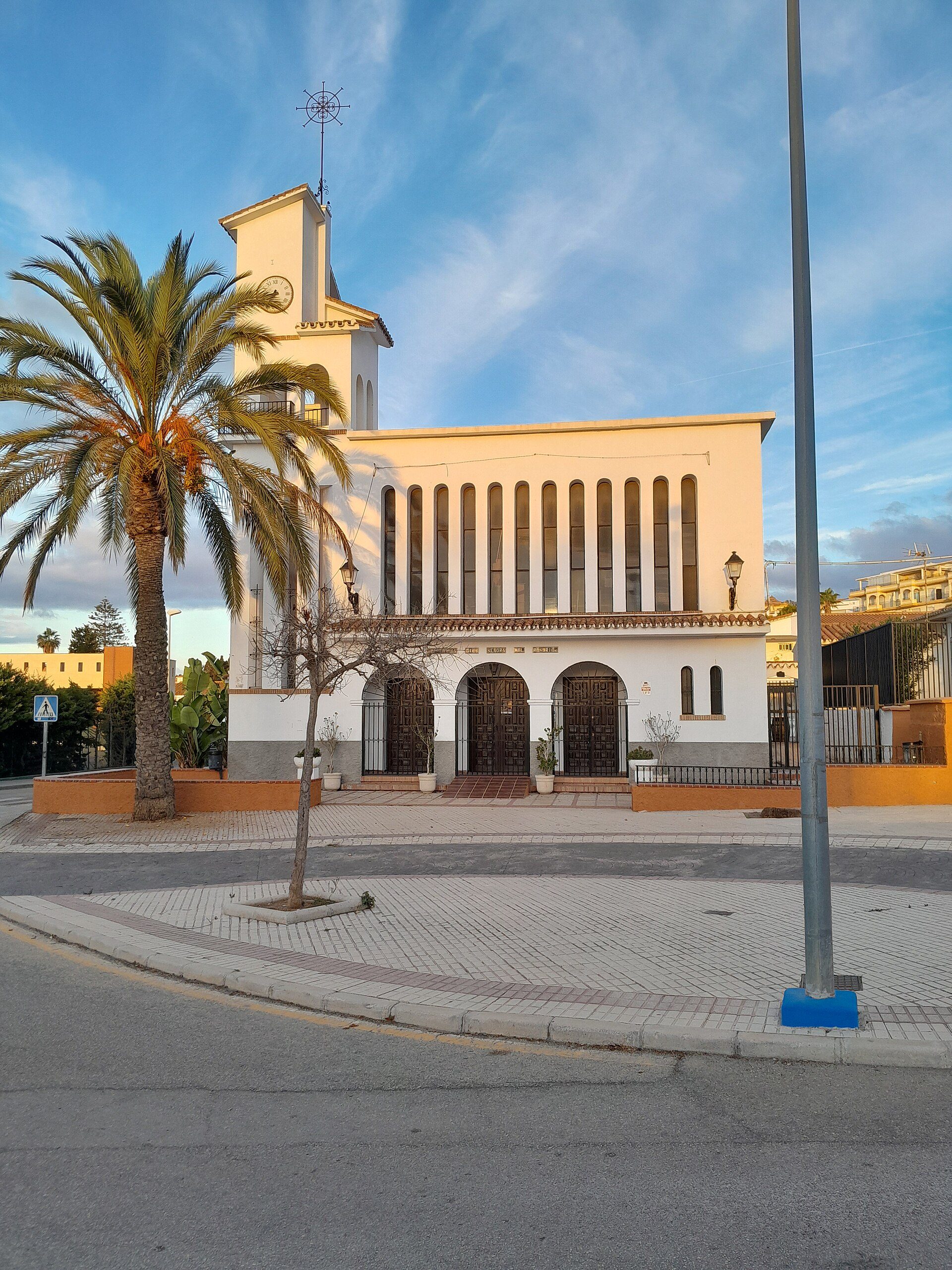 Alt text: White building with palm tree, clock tower, and arched entrance.