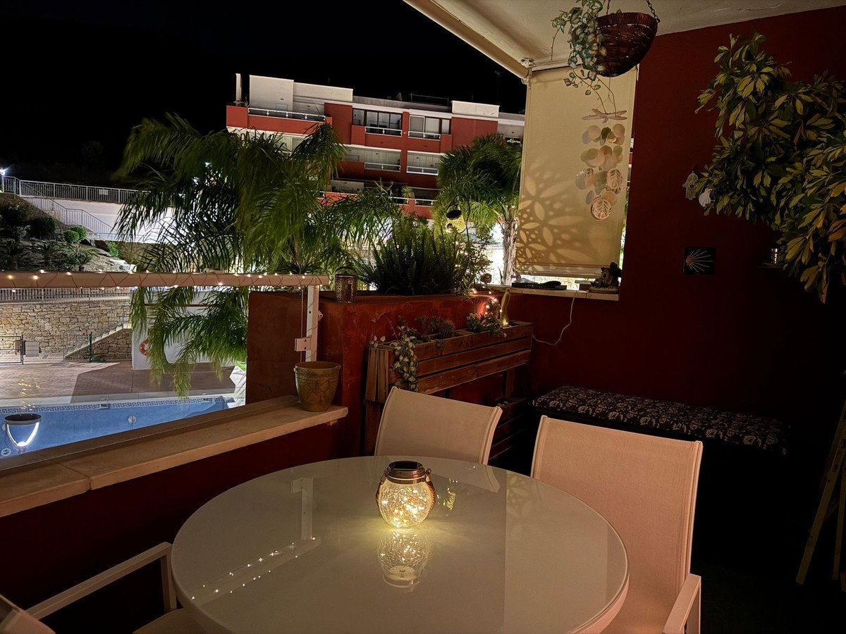 A patio area with a table, chairs, and a bench, overlooking a swimming pool at night.