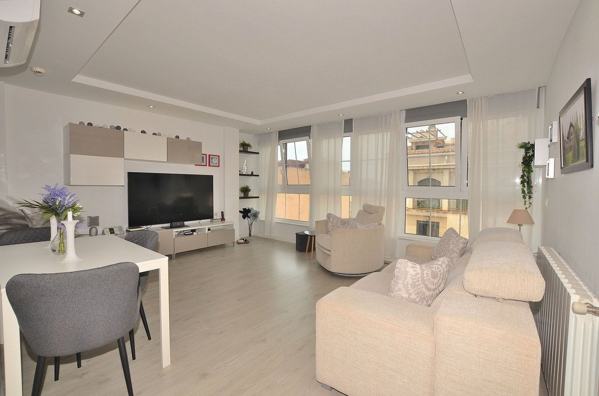 Modern living and dining area with a large television, comfortable sofa, dining table, and bright windows overlooking buildings.