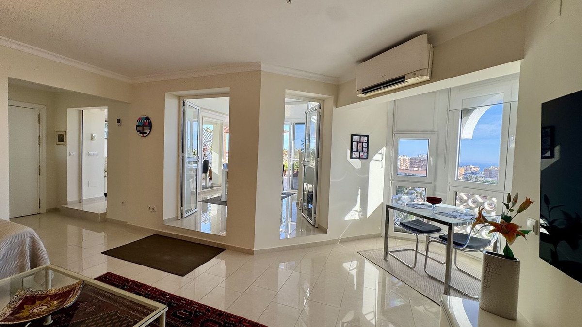 Bright living room with a dining table and chairs, large windows with sea and city views, and access to a balcony.