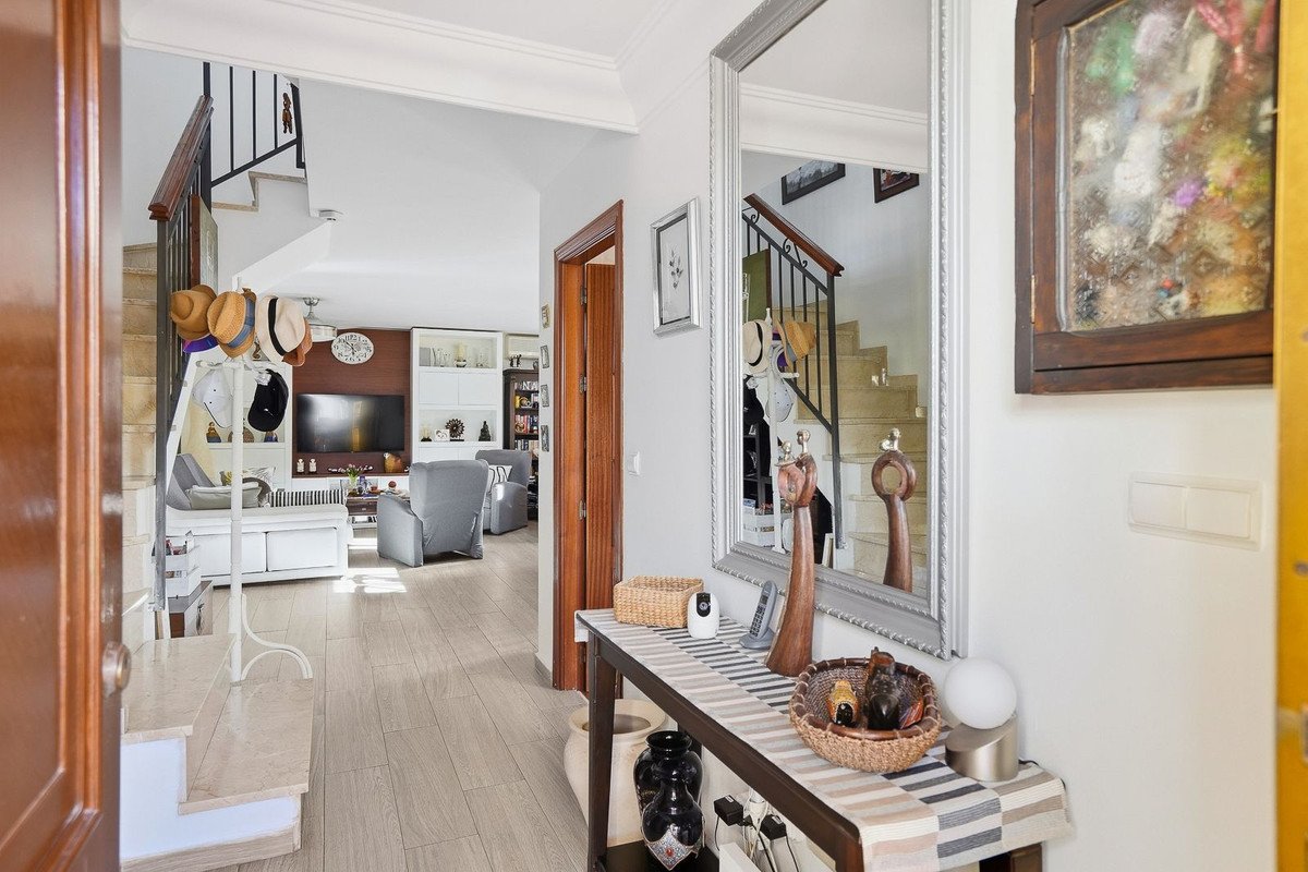 Interior view of a house entrance hall with a staircase, large mirror, and living room visible in the background.