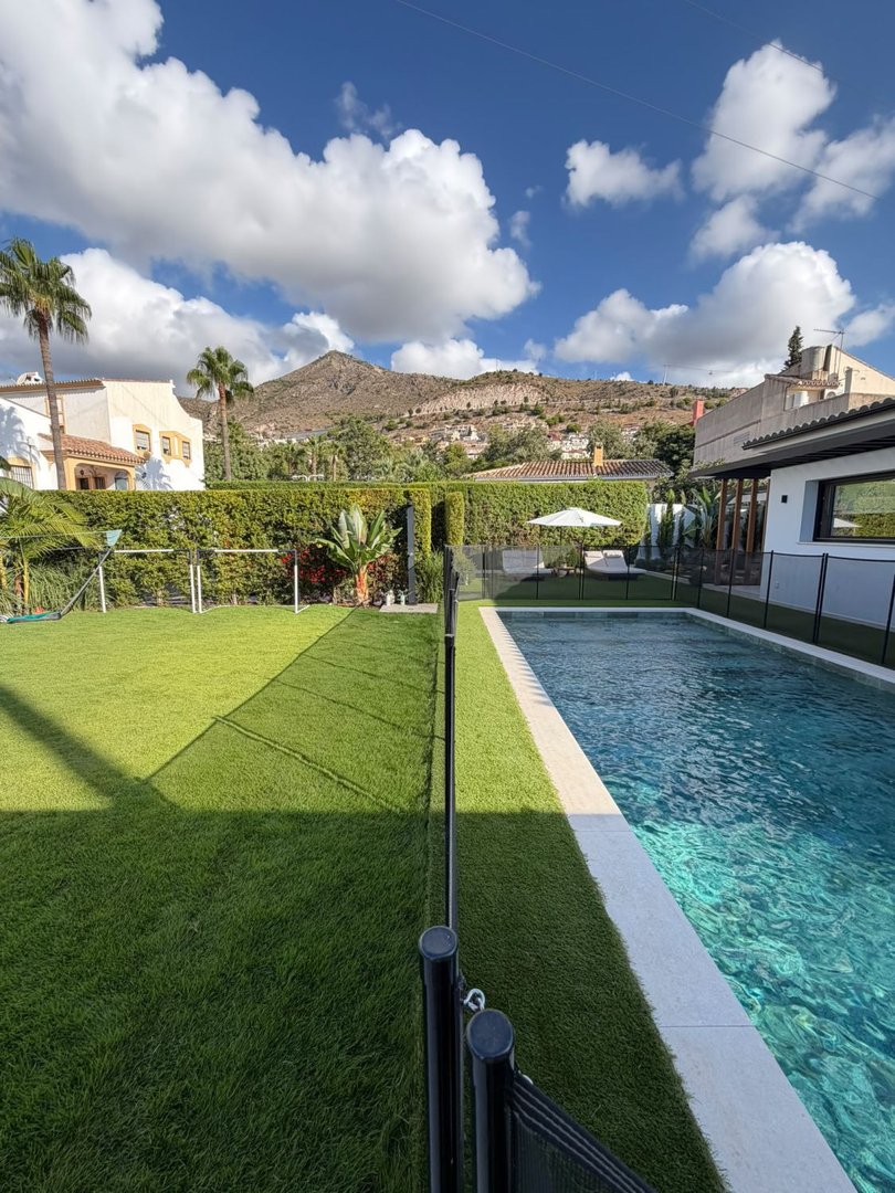 A spacious backyard with a swimming pool, artificial turf lawn, and a scenic mountain view under a cloudy blue sky.