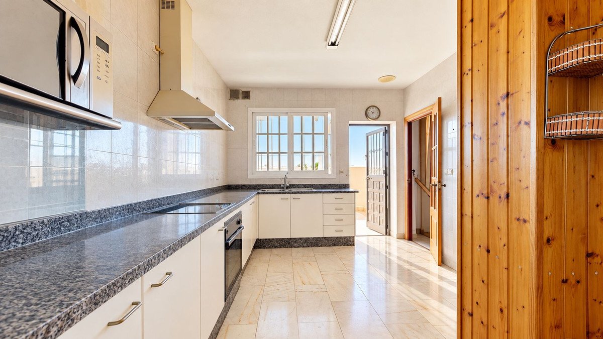 A bright kitchen with white cabinets, granite countertops, and a window overlooking a balcony with outdoor views. Includes a microwave and oven.