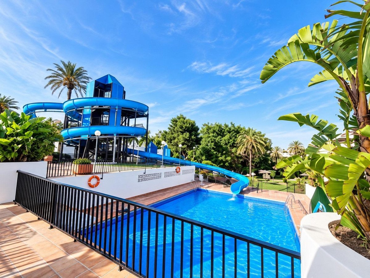 A blue water slide complex next to a bright blue swimming pool surrounded by palm trees and lush greenery.
