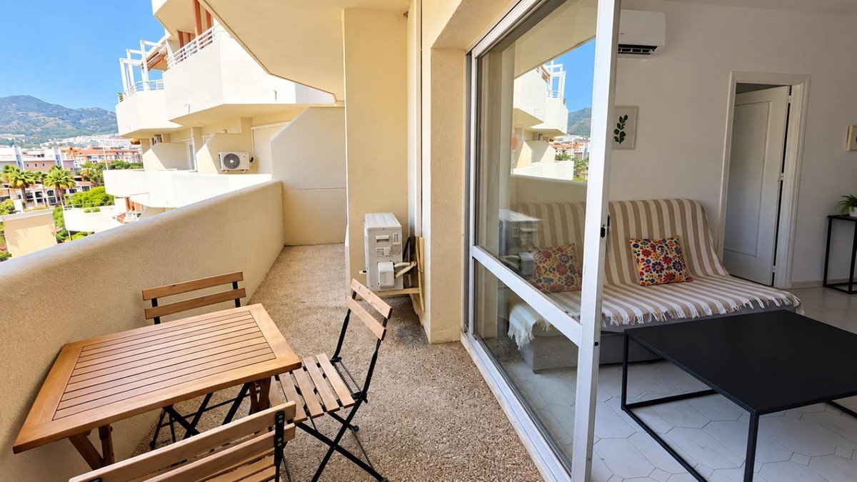 A balcony with a small wooden table and chairs, offering a view of distant mountains and buildings.