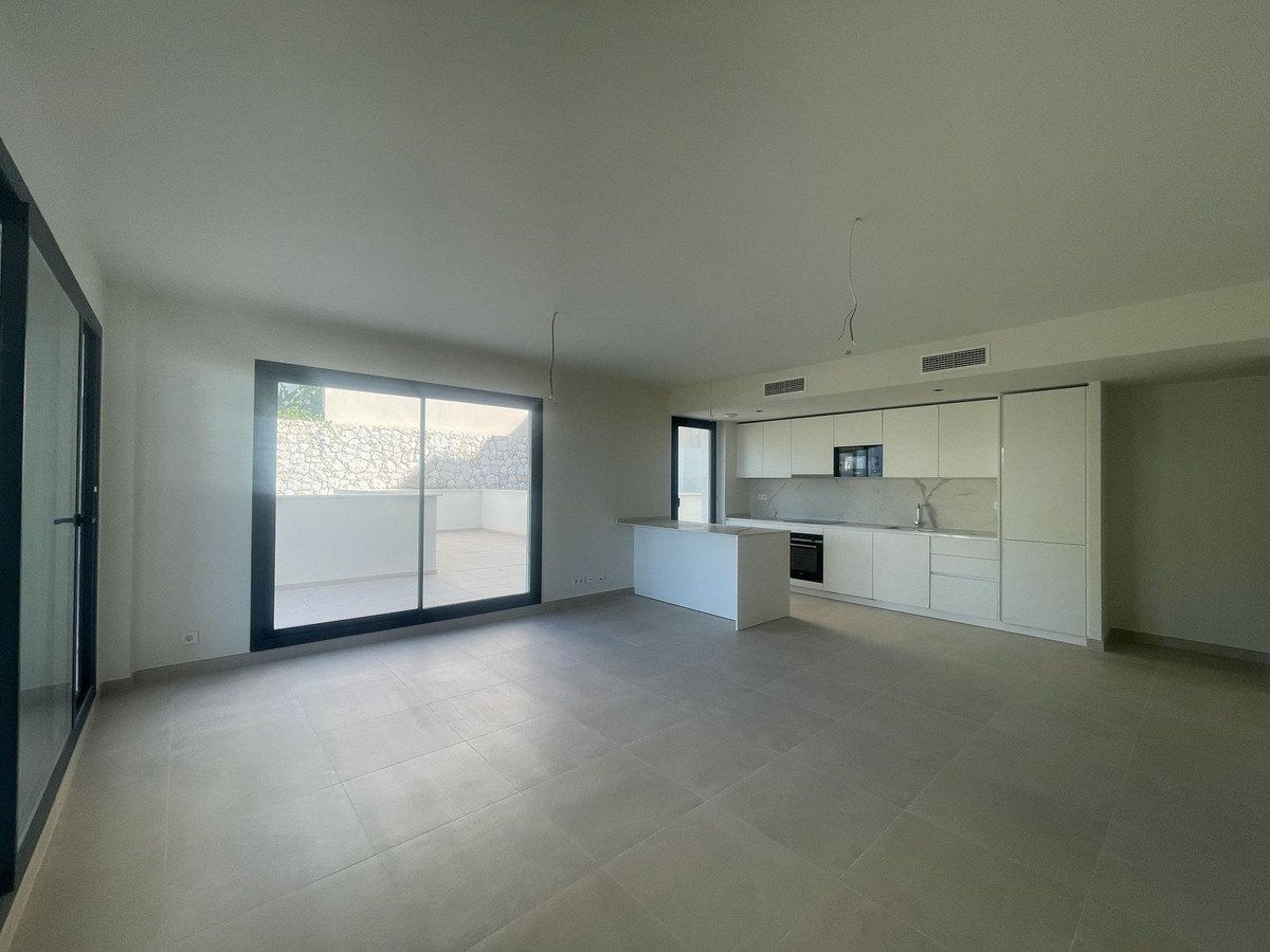 Modern open-plan living area with a sleek white kitchen and a large window overlooking a spacious terrace.