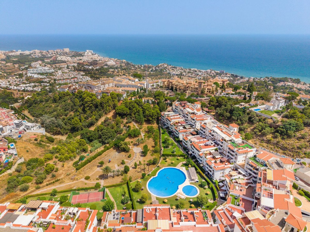 Aerial view of apartments with pool, tennis court, and sea in the background.