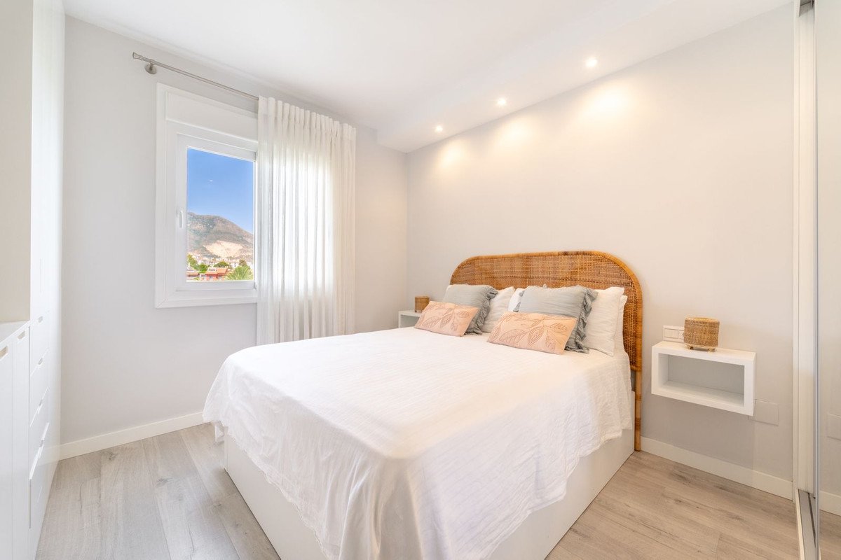 A bedroom with a large bed, wicker headboard, and a window with a view of mountains and the town below.