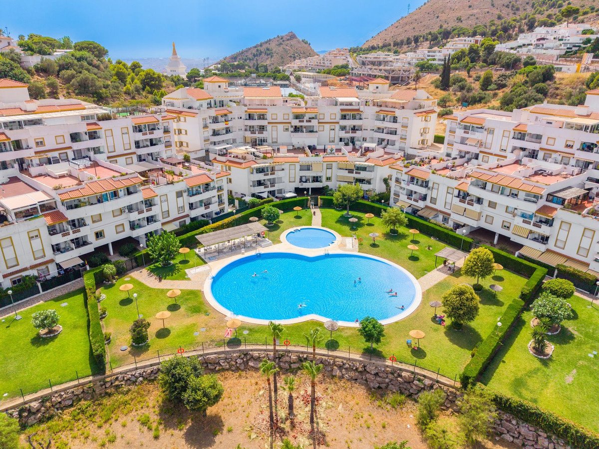 Aerial view of an apartment complex with a large blue swimming pool, surrounded by green lawns and palm trees.