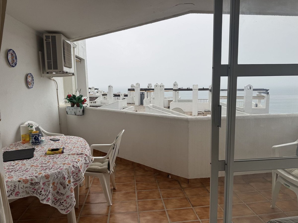 A table and chairs on a balcony with a sea view and white buildings.