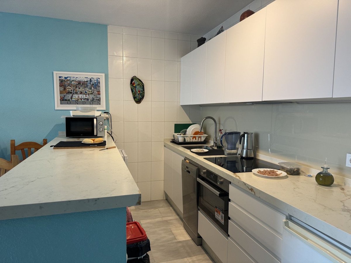 A modern kitchen with white cabinets, granite countertops, and light blue accent wall with a framed city print.
