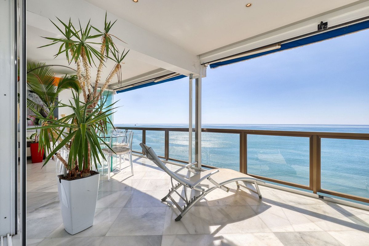 Spacious terrace with a lounge chair and table, overlooking the sparkling blue sea under a clear sky.