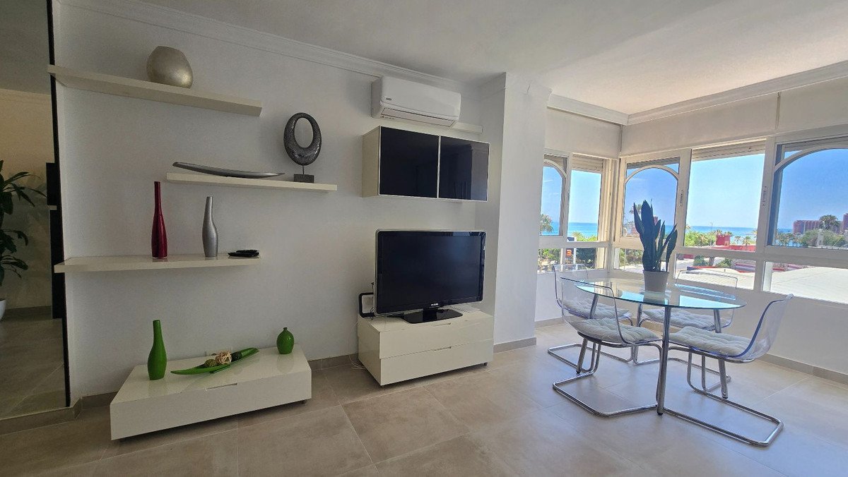 Modern living room with a glass dining table, chairs, and a large window offering a beautiful sea view.