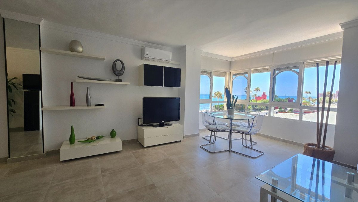 Modern living and dining area with a beautiful sea view through large arched windows, featuring clear chairs and a glass table.