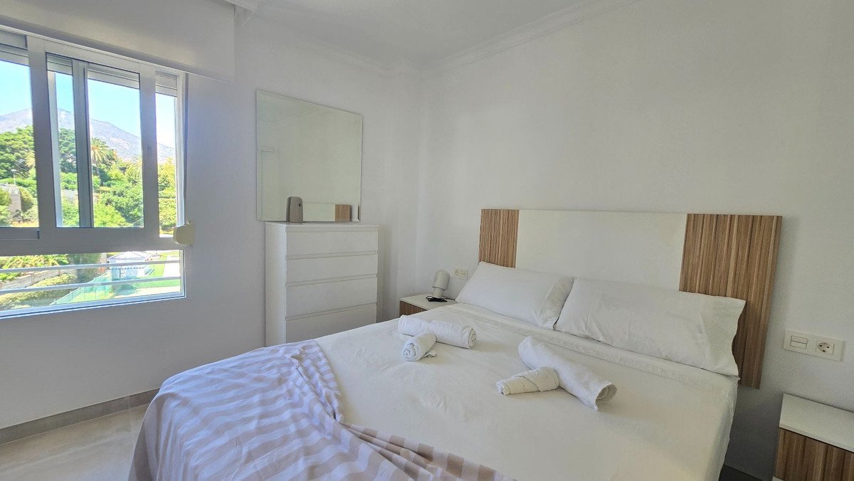 Bright bedroom with a large bed, dresser with mirror, and a window overlooking lush greenery and mountains.