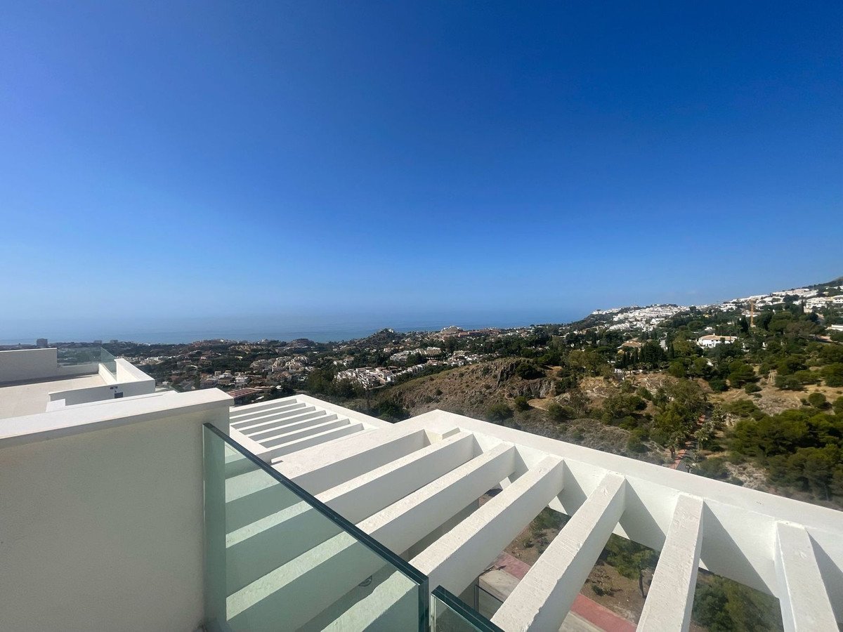 Modern balcony with glass railing offering panoramic views of the sea and hillside town.
