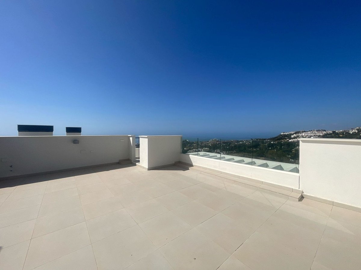 Spacious modern terrace with glass railings offering panoramic sea and town views under a clear blue sky.