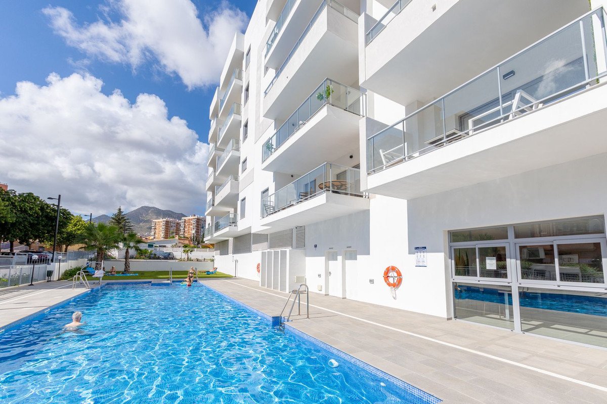 Modern apartment building with balconies next to a large blue swimming pool on a sunny day.