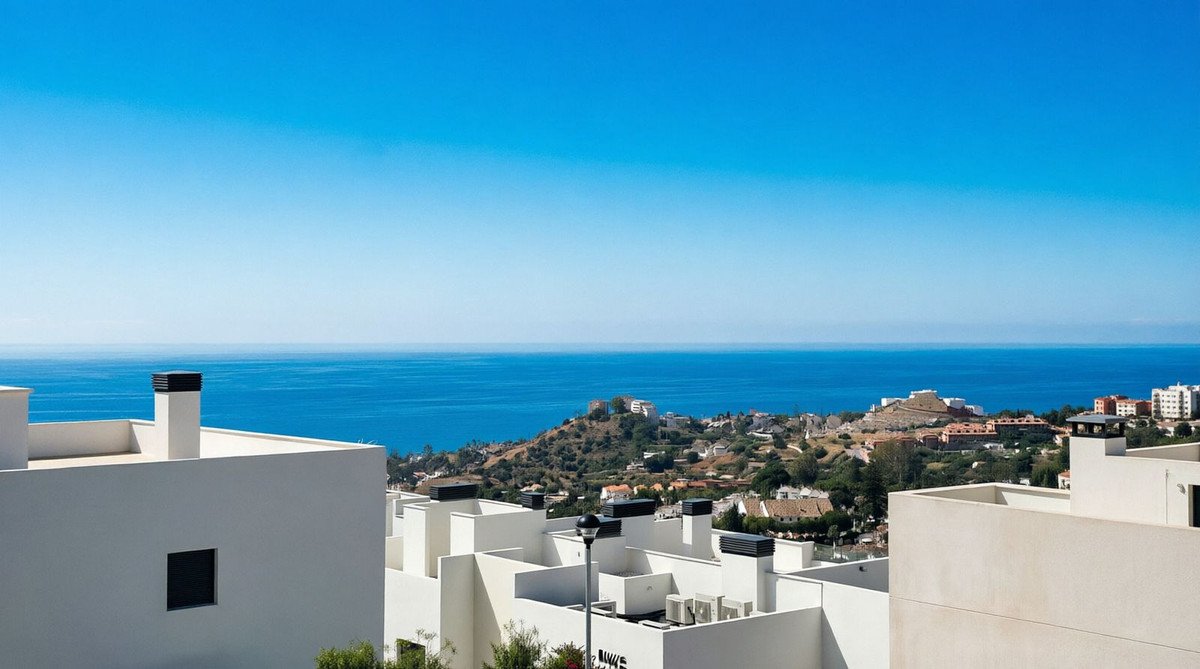 Modern white buildings with a clear blue sea and hillside town view under a bright sky.