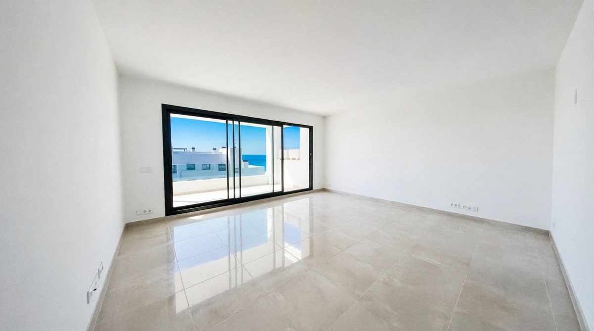 Spacious, empty modern living room with large sliding glass doors leading to a balcony with sea and building views.