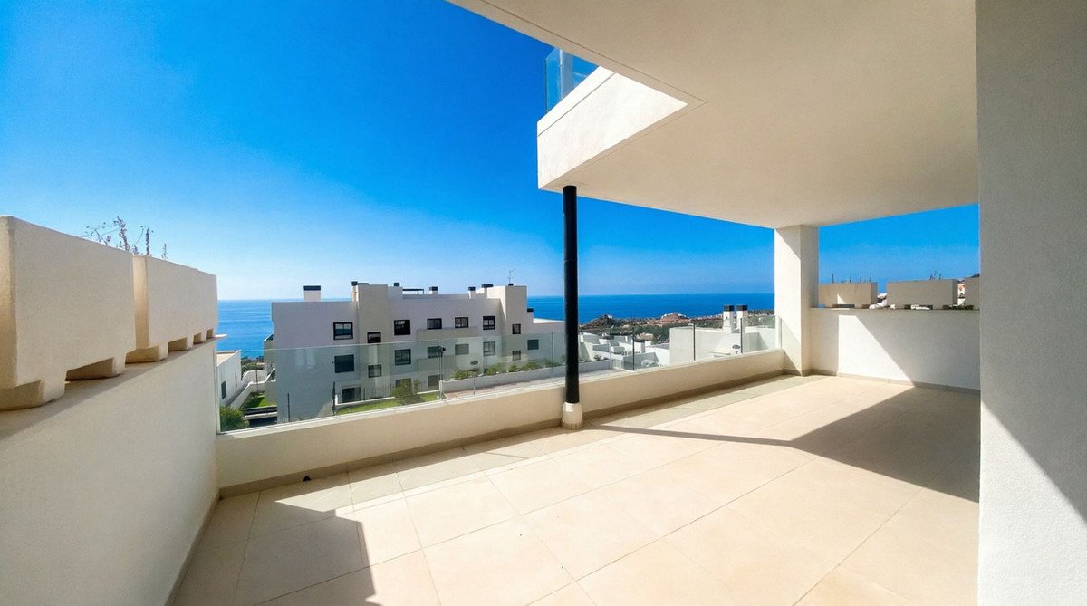 Spacious modern balcony with a stunning sea view, overlooking contemporary buildings under a clear blue sky.