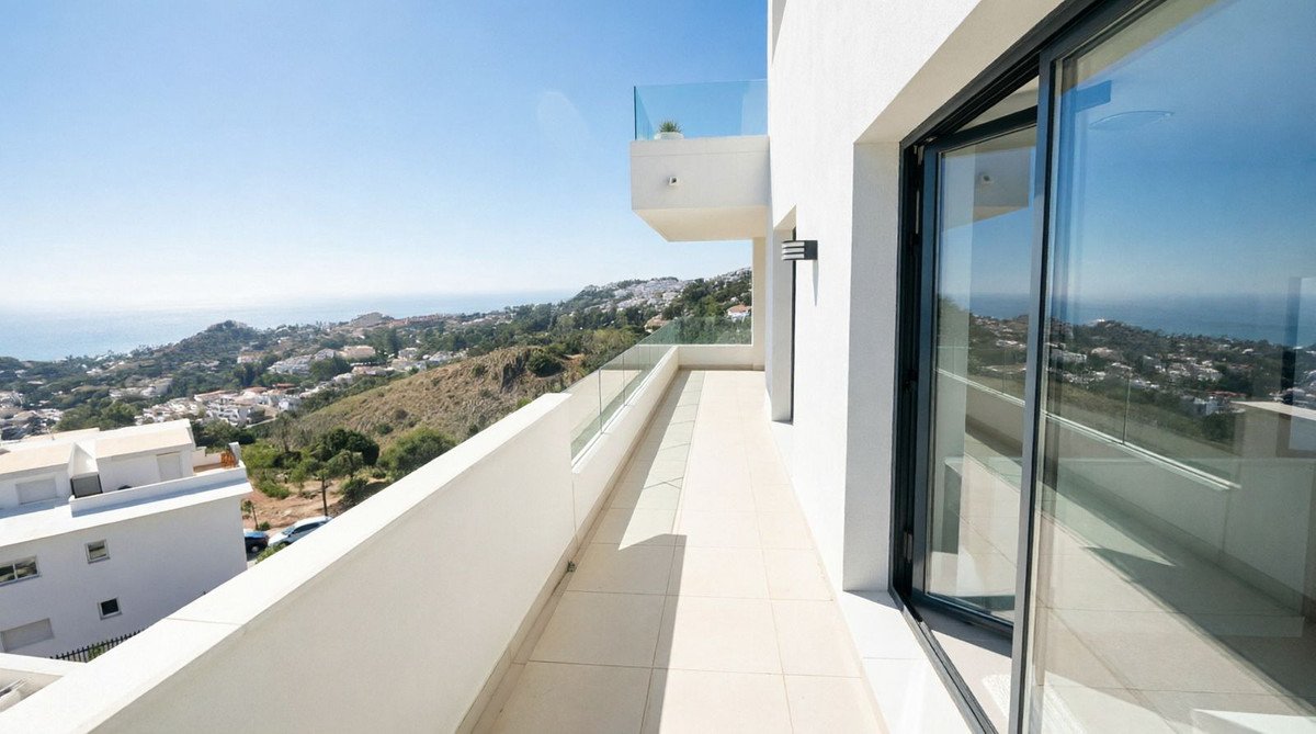 Spacious modern balcony with glass railings overlooking a town and the sea, offering a beautiful panoramic view.