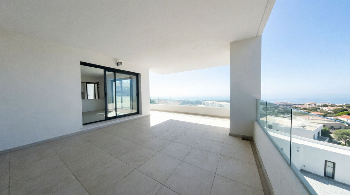 Spacious modern balcony with glass railings and a panoramic view of the sea and coastal town.
