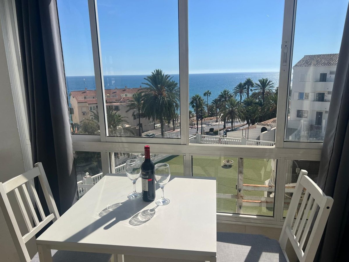 Dining table with wine and glasses set up on a balcony with a stunning sea view and palm trees.
