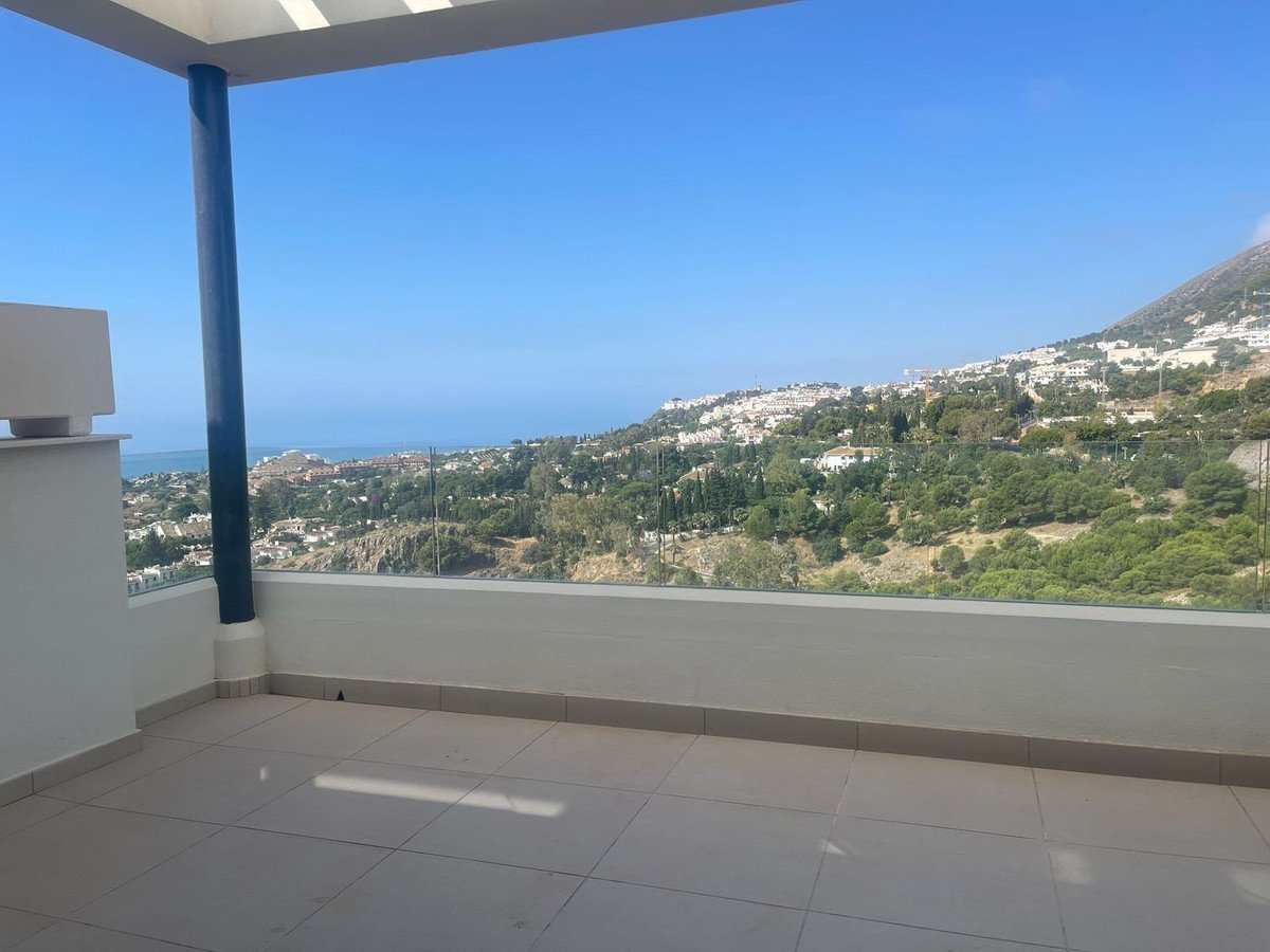 Spacious terrace with glass railings offering a panoramic view of the sea, hills, and coastal town.