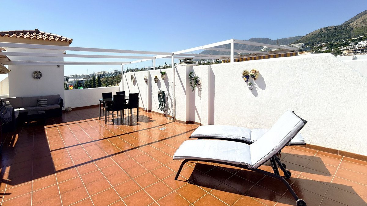 Spacious terrace with dining set, lounge seating, and sun lounger, overlooking a town and mountains under a clear blue sky.