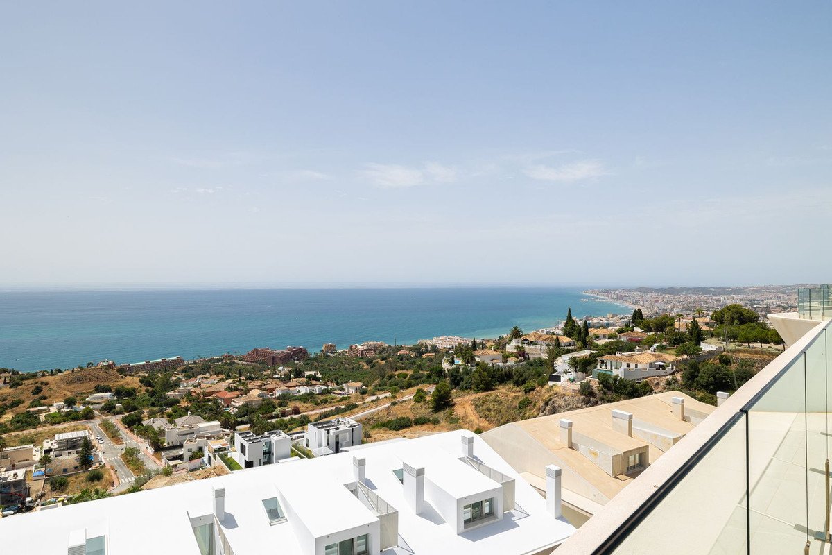 Modern balcony with glass railing overlooking coastal town and blue sea under clear sky.