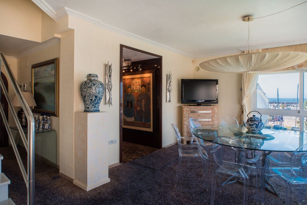 Modern dining area with a glass table, chairs, TV, and a beautiful sea view overlooking a marina with boats.