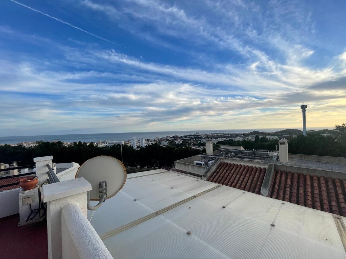 A rooftop terrace overlooks a coastal town with the sea and a dramatic sunset sky in the background.