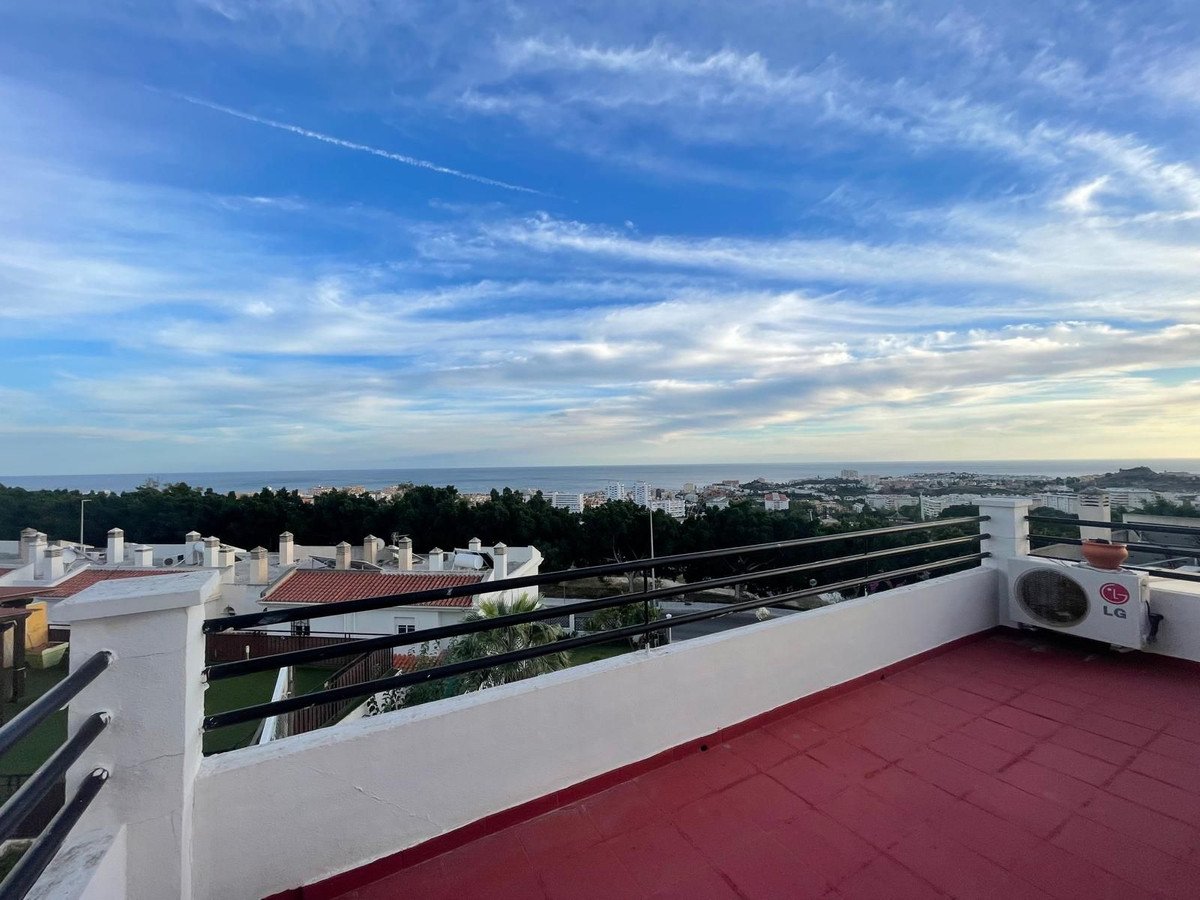 Rooftop terrace with a red floor, overlooking the sea, town, and horizon under a cloudy sky.