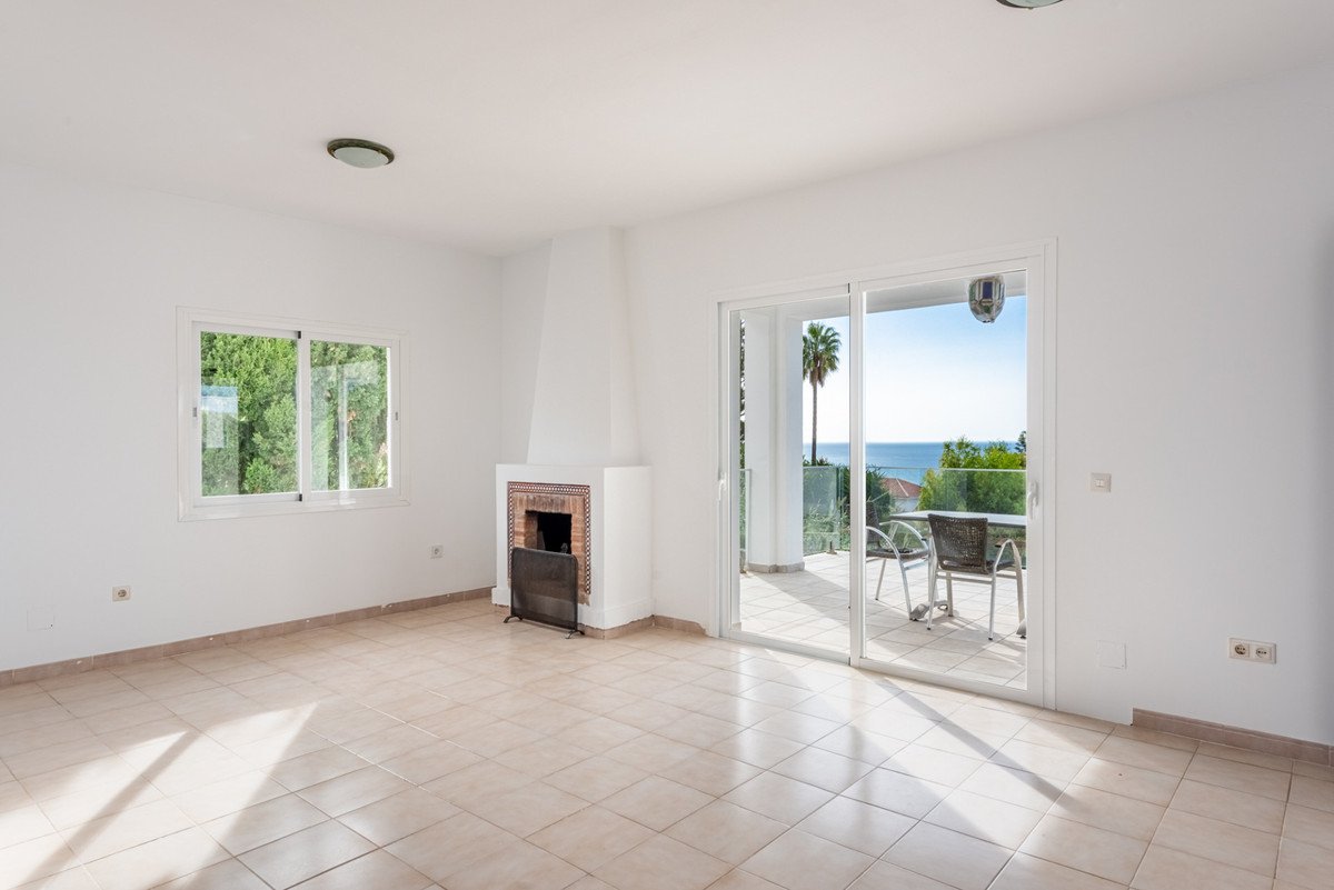 Living room with a fireplace, sliding doors opening to a terrace with sea and palm tree view.