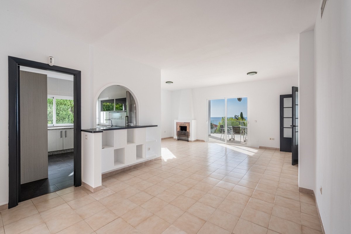 Spacious living room with a fireplace, a view of the sea, and access to a terrace through glass doors.