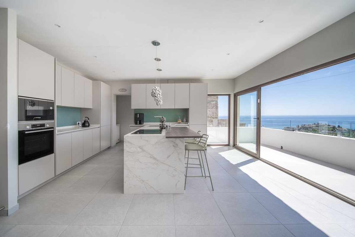 Modern kitchen with island, marble countertops, and a stunning sea view from the balcony.