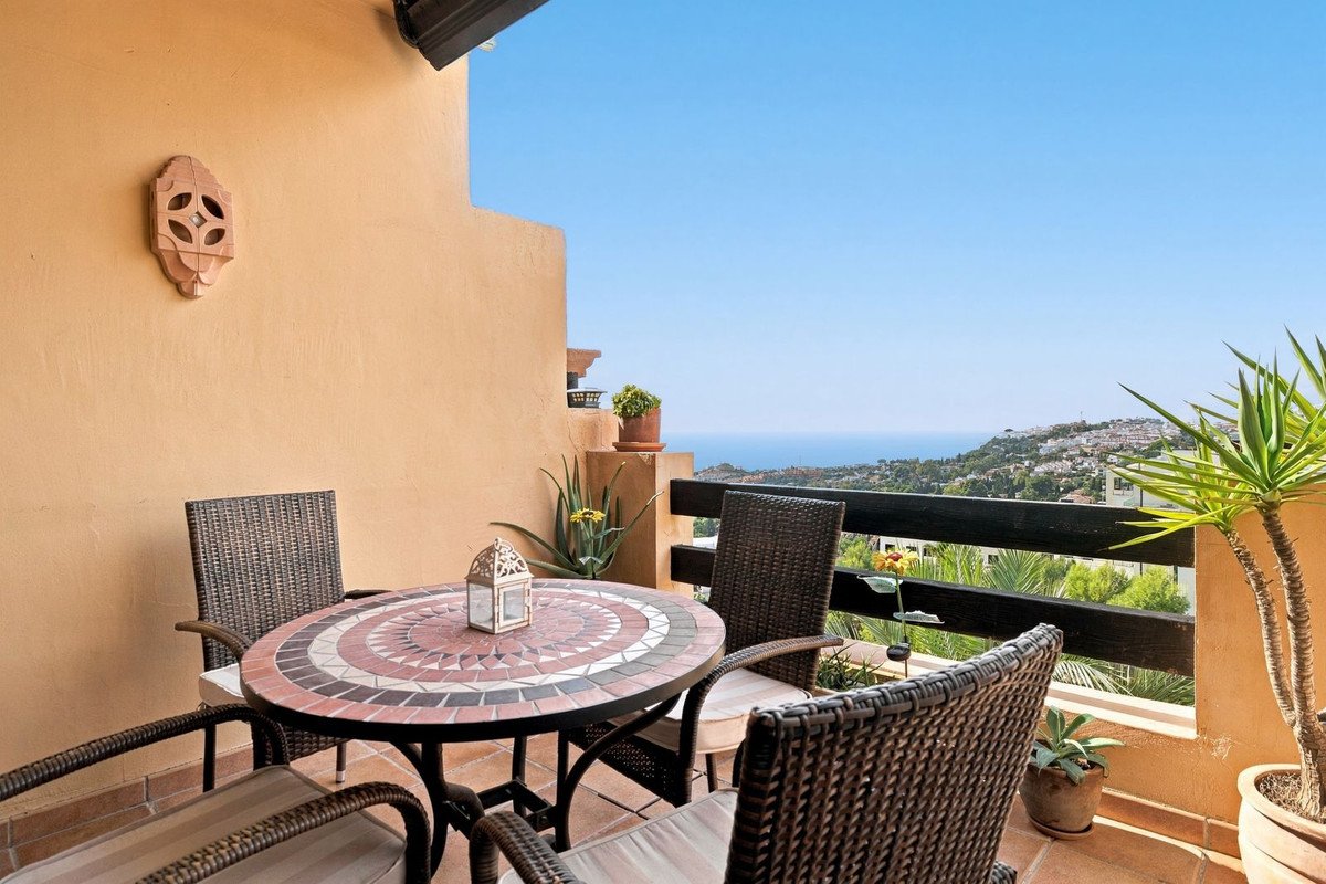 Balcony with mosaic table and chairs, offering a picturesque view of the sea and distant hillside town.
