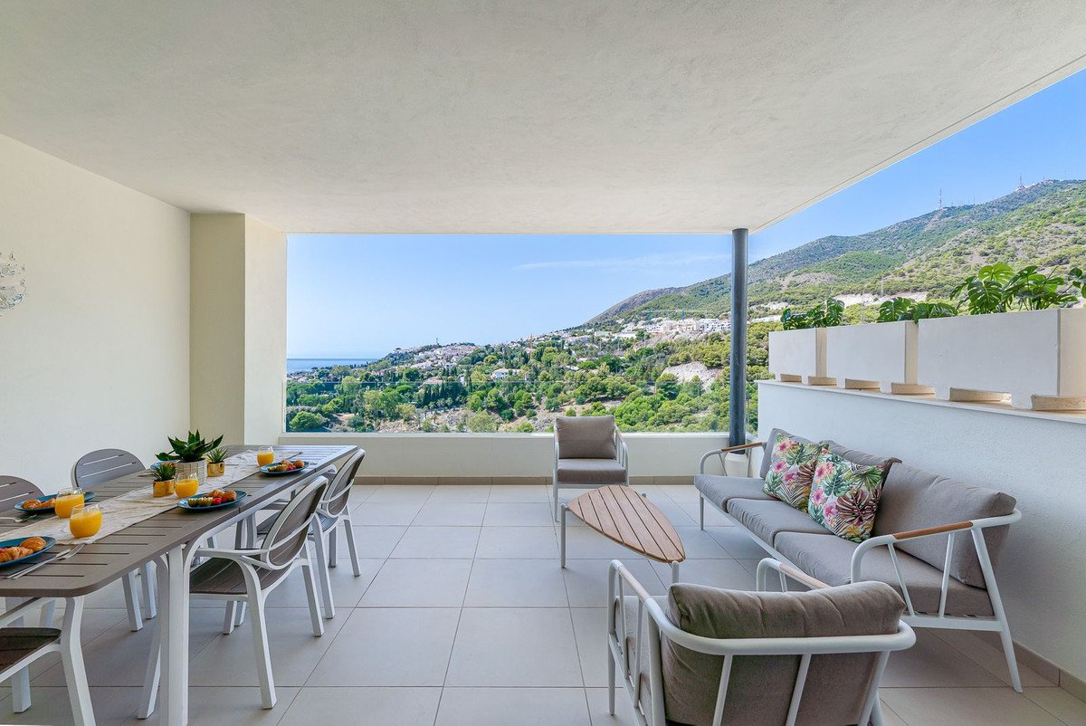Spacious terrace with dining table, seating area, and stunning sea and mountain views under a clear blue sky.