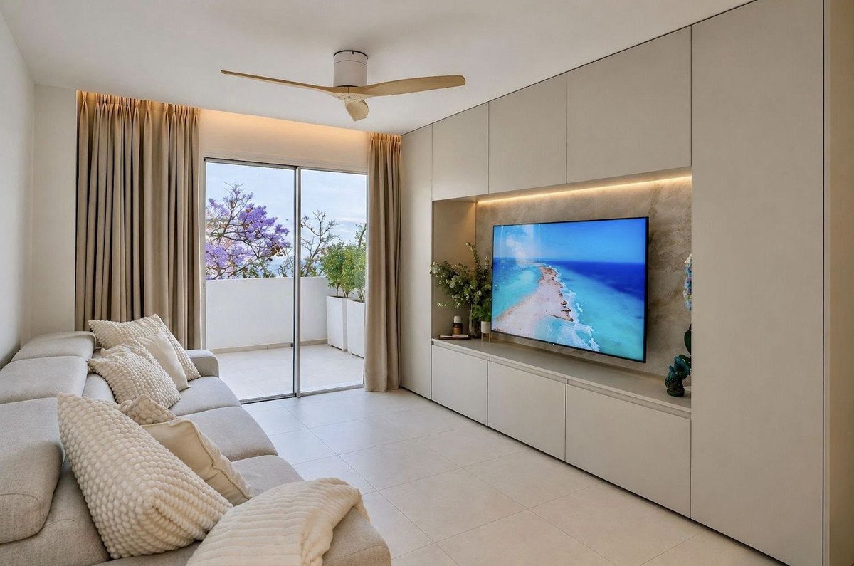Modern living room with a large sectional sofa, entertainment center with TV, and balcony access with a view of trees.