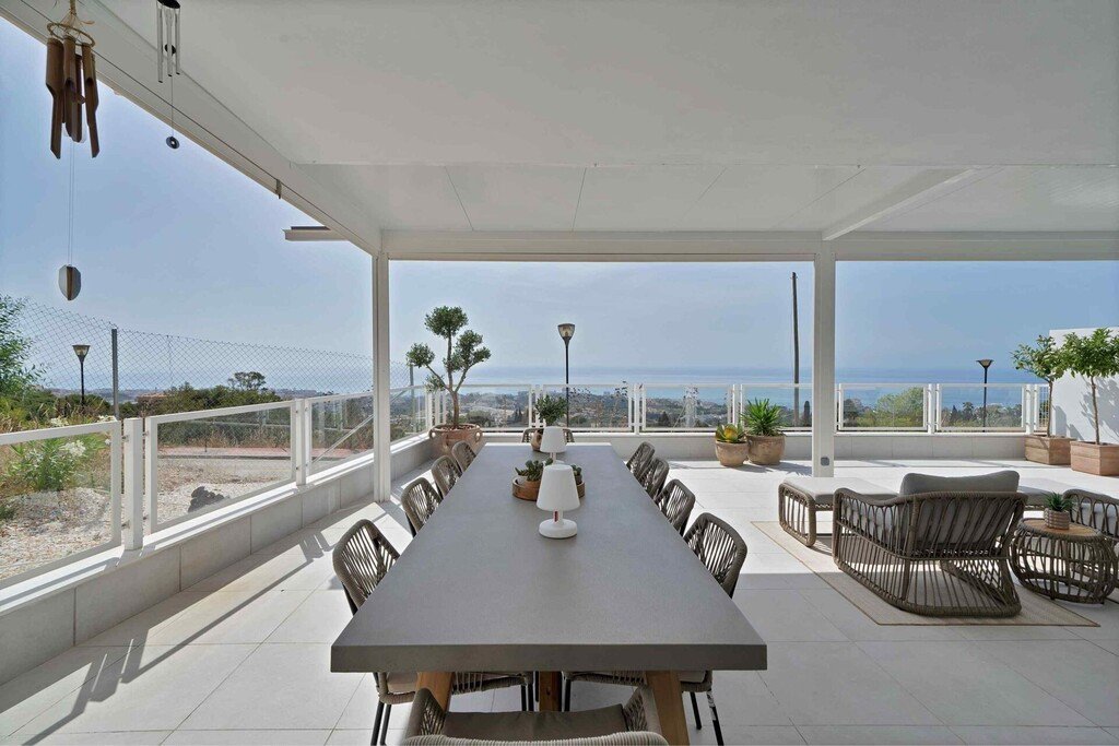 Spacious covered terrace with large dining table, lounge seating, and panoramic sea views.