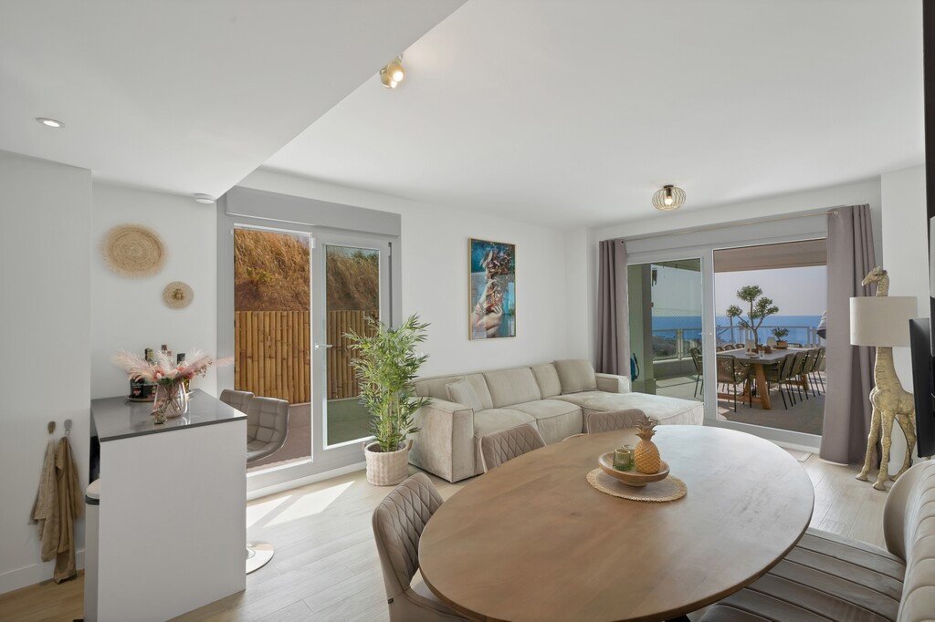 Modern living and dining area with a sectional sofa, oval table, and a terrace with sea views and outdoor dining.