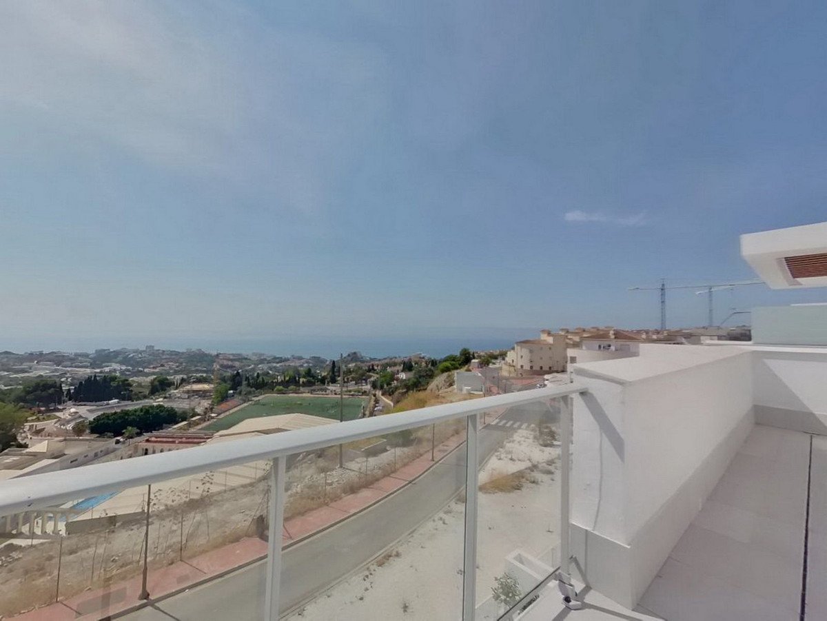 A view from a balcony overlooking a town, a soccer field, and the distant sea under a clear blue sky.