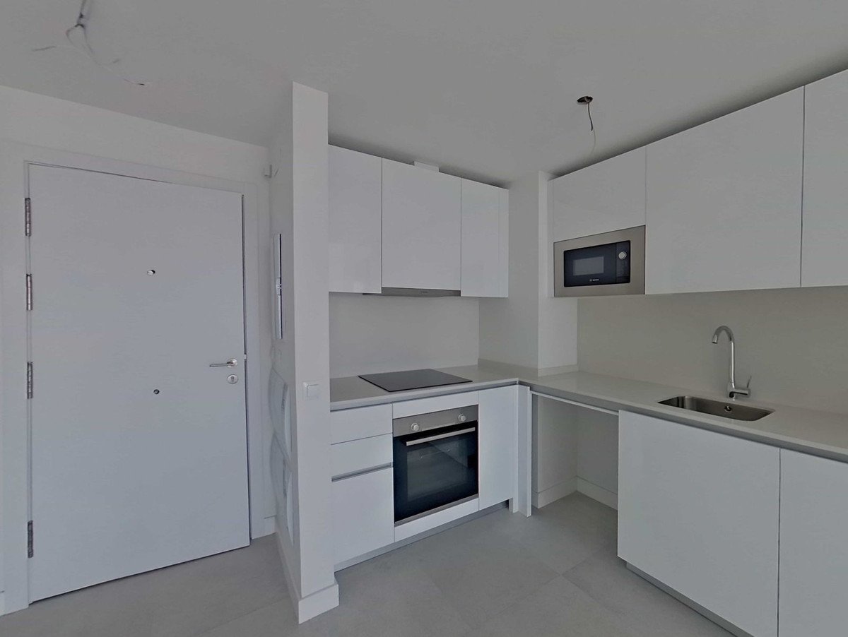 A modern white kitchen with a microwave, oven, hob, and sink. Features sleek cabinetry and a bright, clean aesthetic.