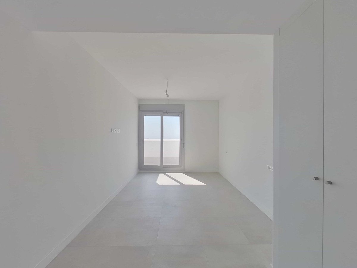 Empty white room with a large sliding glass door offering a bright view and sunlight streaming in.