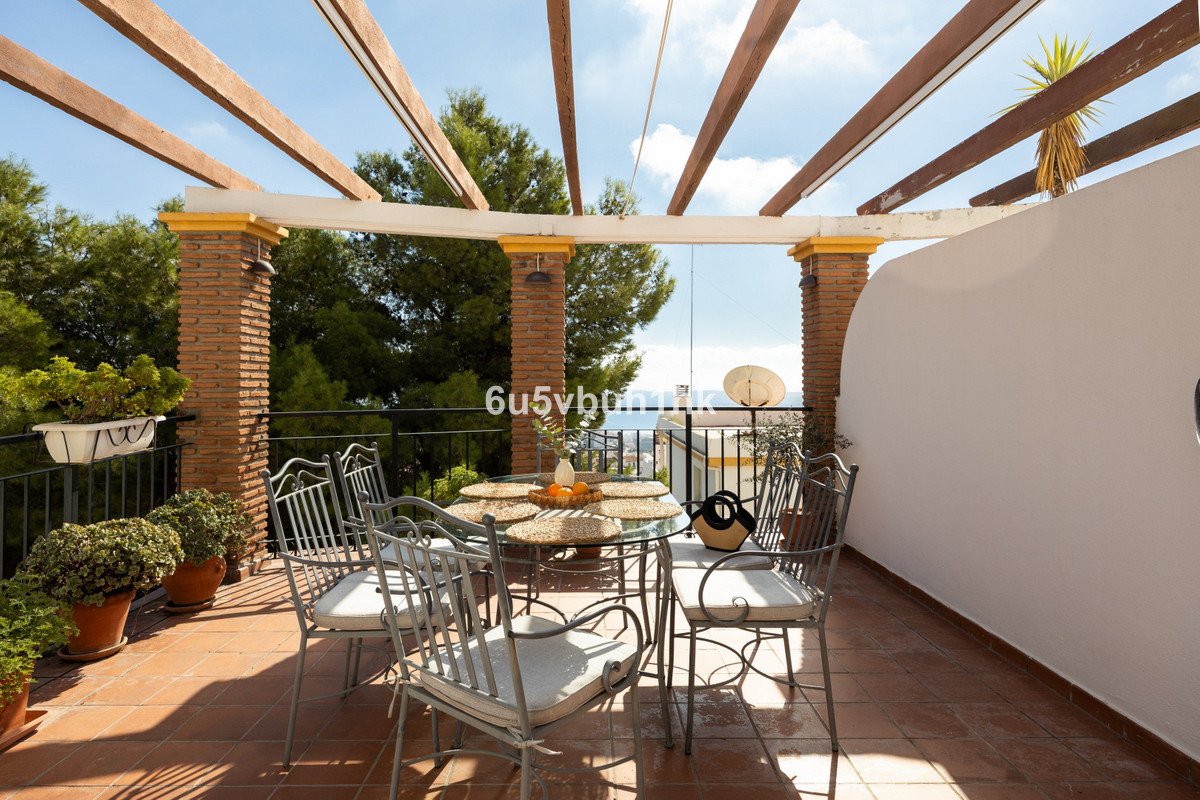 Outdoor terrace with dining set, sea view, and potted plants under pergola