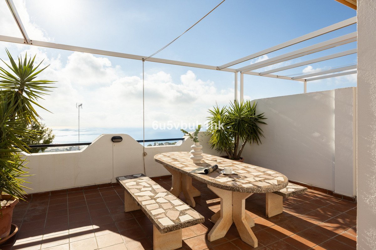 Outdoor terrace with dining table, benches, and sea view under pergola