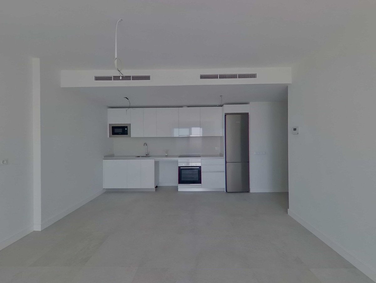 A modern kitchen with white cabinets, microwave, oven, refrigerator, and sleek countertop. Bright and spacious with a minimalist design focused on functionality.